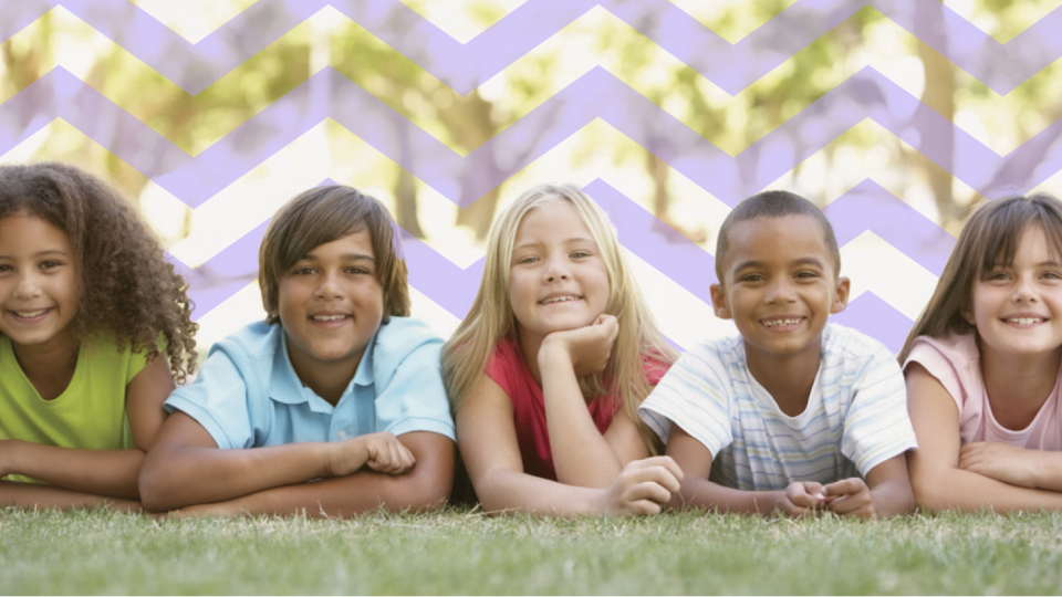 Happy children laying on their stomachs on a lawn.