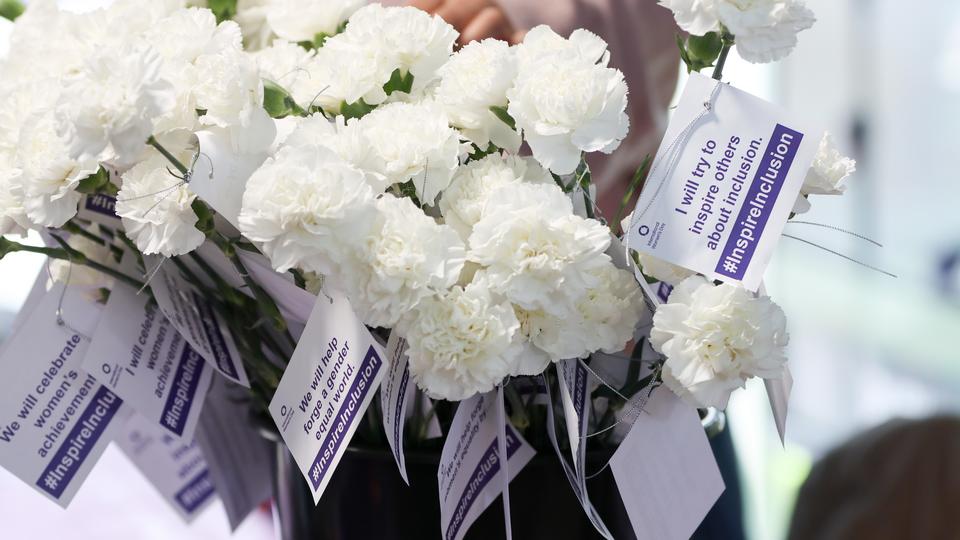 A bunch of white flowers wrapped with International Women's Day promotional postcards