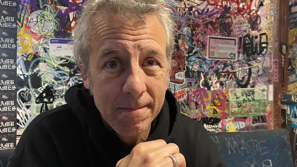 Portrait photo of man in black hoodie in front of colorful board