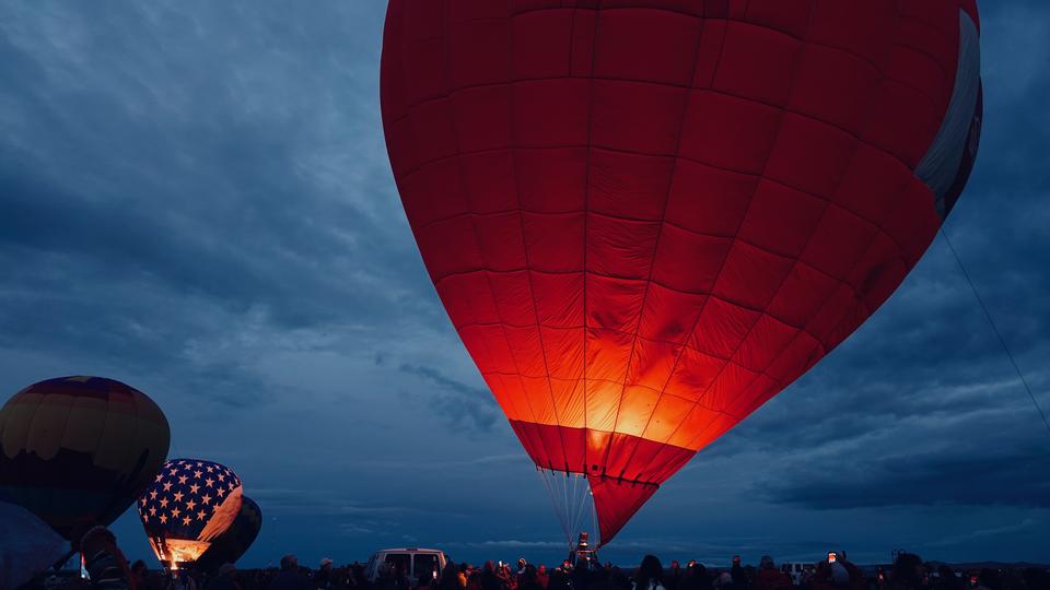 red hot air balloon just off the ground in a field of other balloons at night