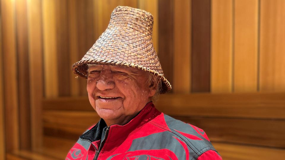 Indigenous man in a red sweater and and a Coast Salish hat. 