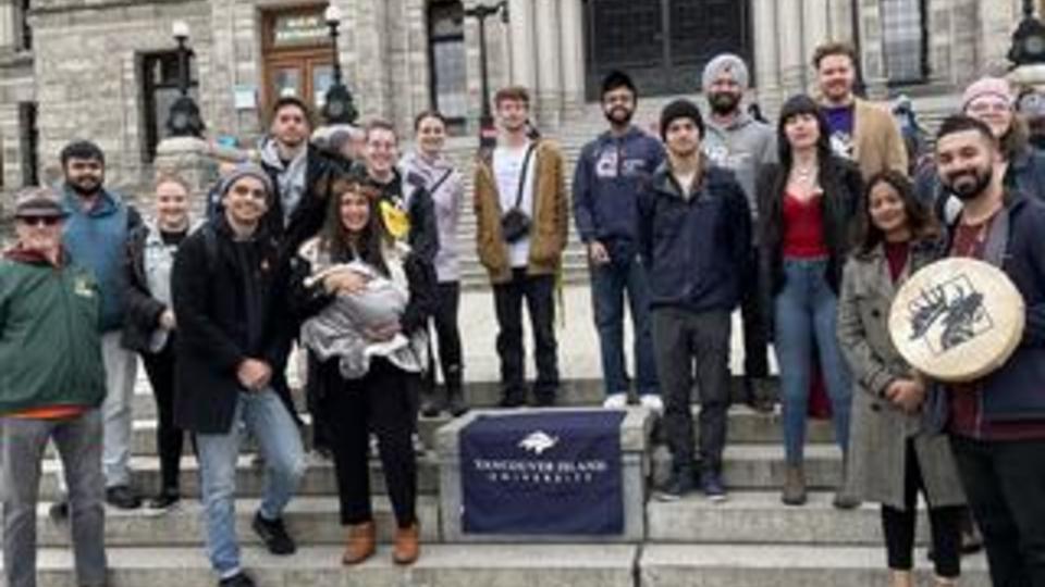 a group of people in front of the legislature in Victoria with a Moose Hide drum and VIU banner