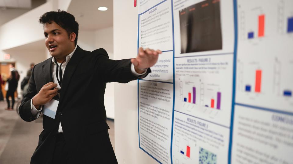 A man standing in front of and presenting an academic poster 