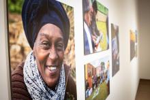 Four photographs hang on the gallery wall. The closest photo is of a person facing the camera smiling.